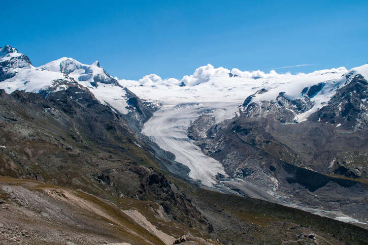 Una valle profonda sopra la quale si ergono le montagne rocciose e innevate delle Alpi svizzere.