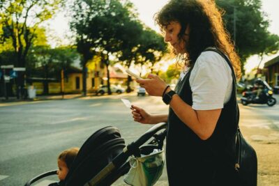 Donna con passeggino che guarda il telefono, simbolo dell’equilibrio tra lavoro di cura e vita digitale nel contesto del divario di genere.